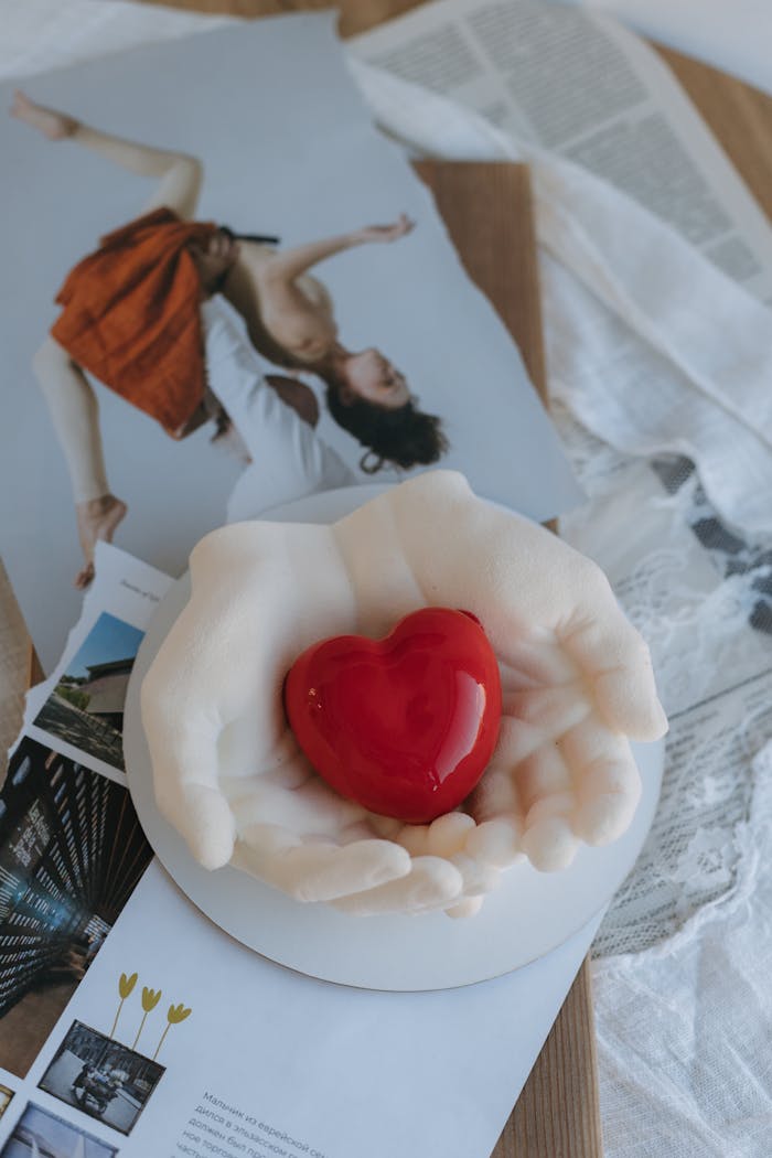 A creative flat lay featuring a sculpture of hands holding a heart on a backdrop of artistic photographs.